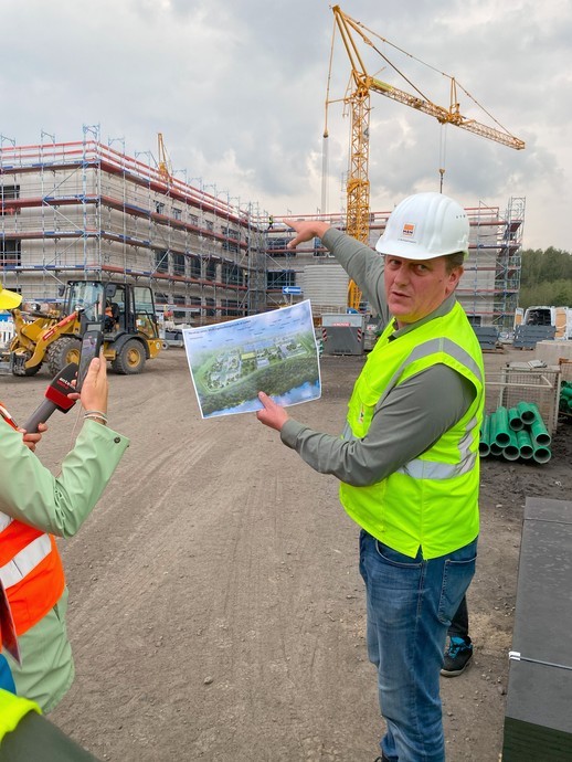 Ein Mann mit Bauhelm und Leuchtweste steht mit einem Plan vor einem eingerüsteten Gebäude und erklärt. (Bild: LWL/Schufi) (vergrößerte Bildansicht wird geöffnet)
