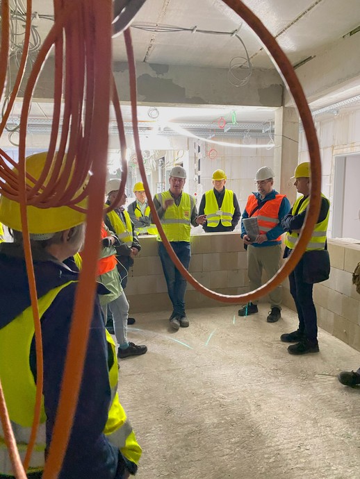 Eine Gruppe von Menschen in Bau-Schutzkleidung steht in einem Raum im Rohbau, an dem große Fensteröffnungen erkennbar sind. (Bild: LWL/Schufi) (vergrößerte Bildansicht wird geöffnet)