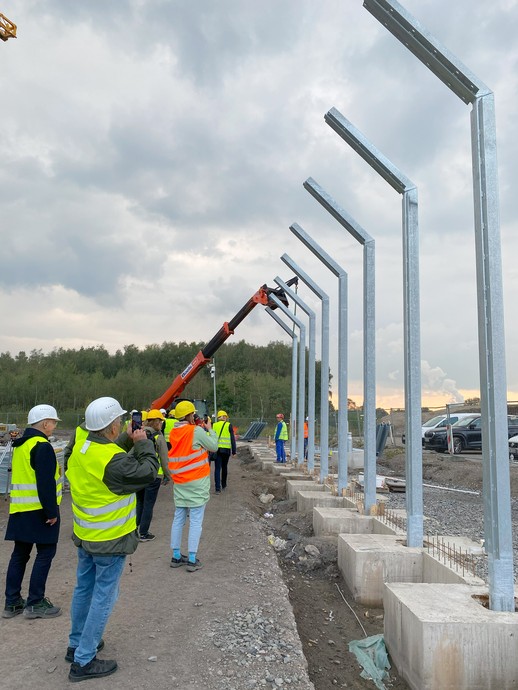 Eine Gruppe von Menschen steht vor hohen, oben nach innen gebogenen Stahlpfählen (Bild: LWL/Schufi) (vergrößerte Bildansicht wird geöffnet)