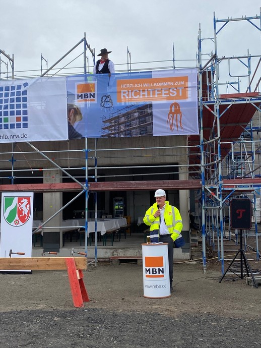 Ein Mann in gelber Baustellenjacke steht neben einem Nagelbalken und spricht in ein Mikro. (Bild: LWL/Schufi) (vergrößerte Bildansicht wird geöffnet)