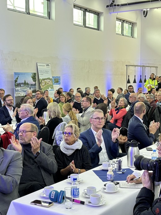 Blick in einen großen Raum mit applaudierenden Menschen an Tischreihen. (Bild: LWL/Schufi) (vergrößerte Bildansicht wird geöffnet)