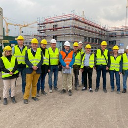 Eine Gruppe von Menschen in mit Bauhelmen und Leuchtwesten steht auf einer Baustelle vor einem großen eingerüsteten Gebäude. (Bild: LWL/SchuFi)