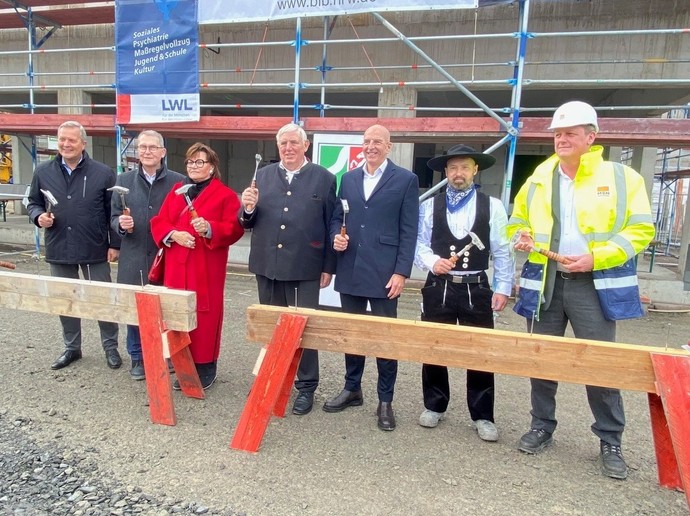 Mehrere Männer und eine Frau stehen hinter einem Balken mit großen Nägeln und präsentieren Hämmer. (Bild: LWL/SchuFi)